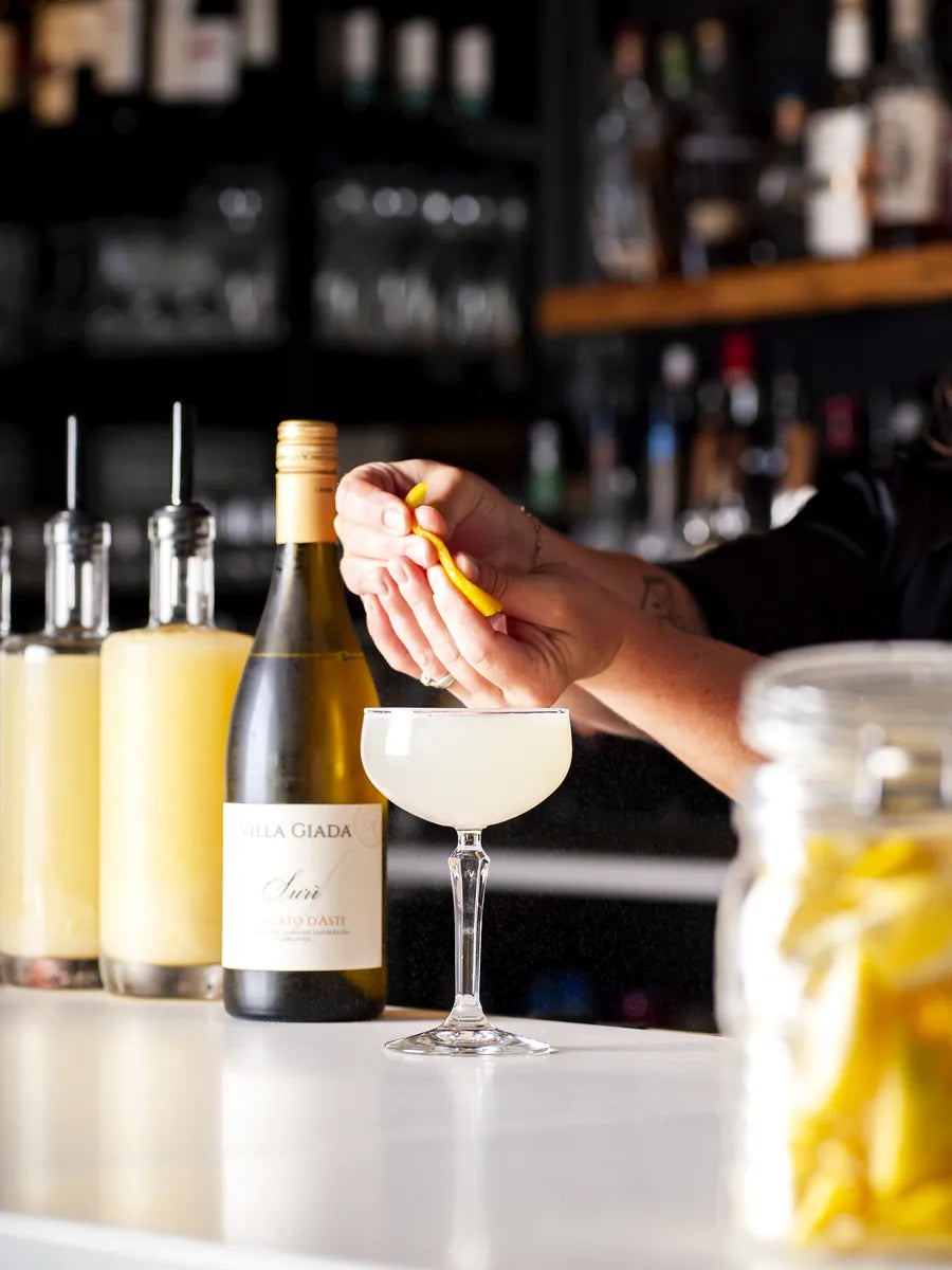 A Prost bartender finishing a cocktail with a citrus garnish